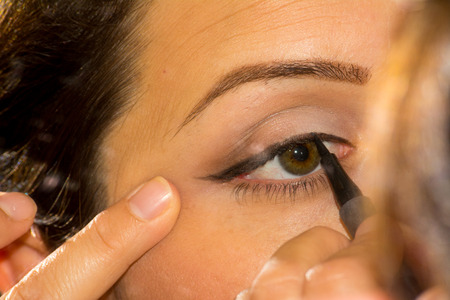 Close Up of Woman Stretching Skin Using Eye-liner on Blur Backgroundの写真素材
