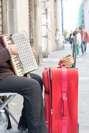 Close Up of Old Beggar Woman Playng a Dirty Accordion in the Street near a Red Suitcase on Blur Backgroundの写真素材