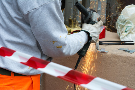 Worker using an Orbital Grinder on Steel Surface wearing Orange Work Trousers and Safety Tools