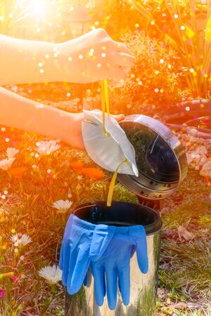Girl that trows blue gloves and medical mask in the trash after the covid 19 emergency on sun flares and glittered background. Concept of post emergency. Return to normal life. Come back to normality. Stop of Pandemicの写真素材