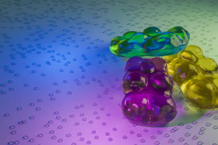 Horizontal View of Close Up of Three Colored Teddy Gummy Candies on White Table with Water Drops on Soft Light Backgroundの写真素材