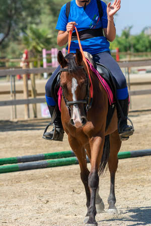 Little girl that rides a brown pony during Pony Game competition at the Equestrian School on blurred backgroundの写真素材