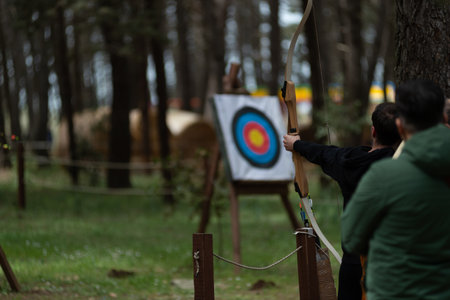 People Performing Archery In The Forest During A Party On Blurred Background