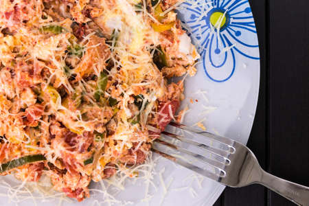 A photo of an omelette with cherry tomatoes, parsley. and grated cheese, shot from above on a rustic wooden texture with a fork and a place for textの写真素材