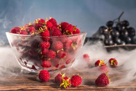 Raspberry in a glass bowl on a wooden table with grapesの写真素材