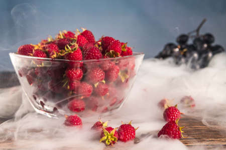 Raspberry in a glass bowl on a wooden table with grapes