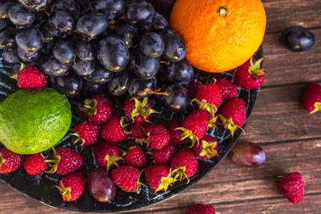 close-up of fruit salad with raspberries, grape, lime on a clay plate on a rustic wooden table,...