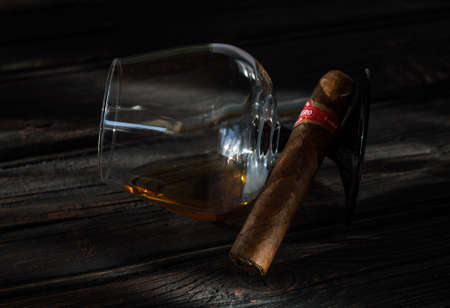 Glass of brandy and cuban cigar on an old wooden table.