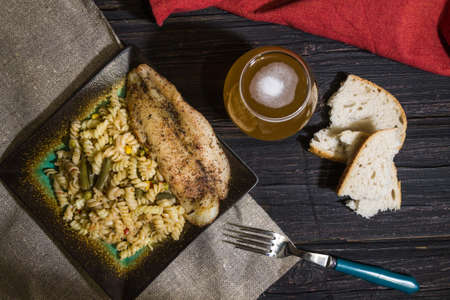 Pasta with delicious, juicy fish, beer and bread on wooden background