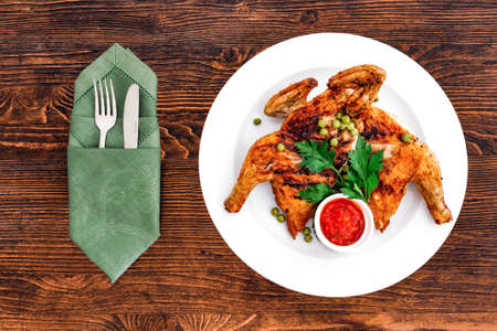 Grilled fried roast Chicken Tabaka on a plate on a wooden background, top view with appliancesの写真素材