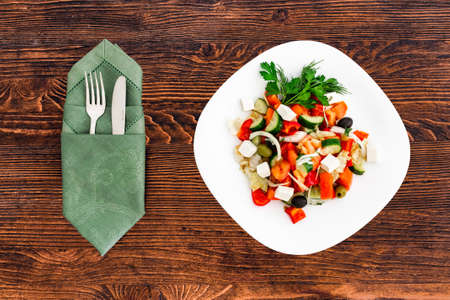 Greek salad of fresh cucumber, tomato, sweet pepper, lettuce, red onion, feta cheese and olives with olive oil. Healthy food, top view with appliancesの写真素材