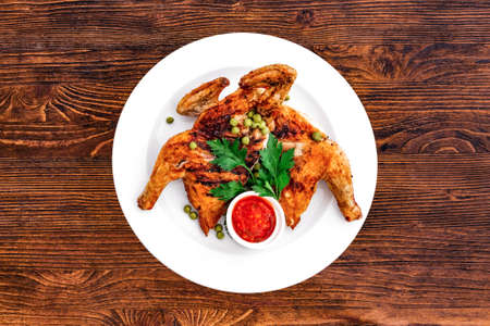 Grilled fried roast Chicken Tabaka on a plate on a wooden background, top viewの写真素材