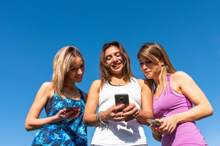 Three happy young women watching the smart phone with a blue sky