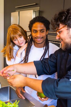 Stock vertical photo of a group of three people of different ethnicities in front of a kitchen sink to wash their hands with a mangoの写真素材