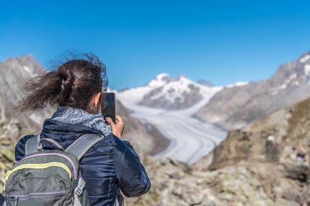 Rear view of woman photographing Aletsch Glacier with smartphone from Eggishorn viewpointの写真素材