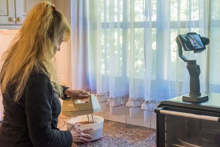 Adult woman filming herself preparing the dough with a mixer for a cake during quarantine.