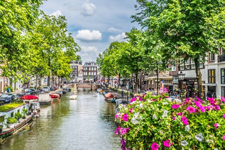 View of one of the canals in Amsterdam. Very flowery bridge and many tourists in the streets on a summer afternoon.の写真素材