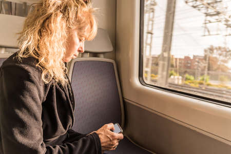 Adult woman traveling alone on the train looking at a mobile. Concept of new naturallyの写真素材