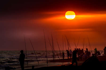 Fishermen with their fishing rods ready to fish on a sunset at the seashoreの写真素材