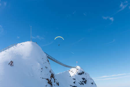 Two mountains with suspension bridge linking them with a person in the sky paragliding over Diablerets Glacier 3000の写真素材