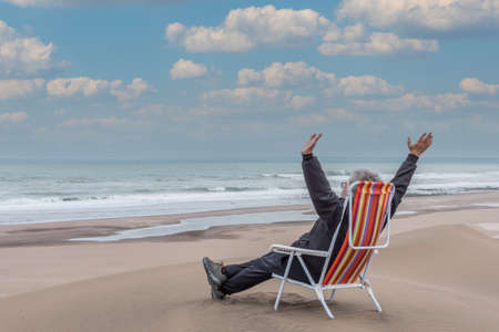 Adult male reclining on a beach lounger in front of the sea with his arms in the airの写真素材