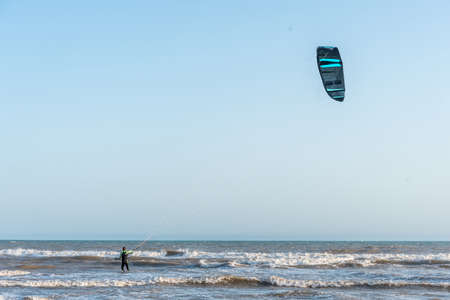 View of an unrecognizable man kitesurfing in the waves with a blue sky.の写真素材