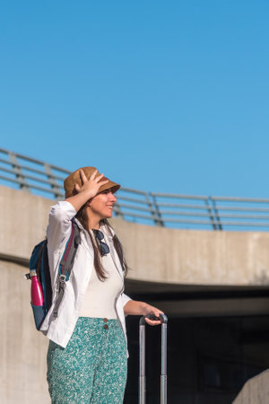 Tourist woman looking away while standing outdoors with suitcase and backpack.の写真素材
