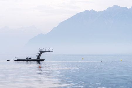 Platform with a ladder and a springboard in a lake Leman, Switzerland with a Alps mountain landscape on a misty day.の写真素材