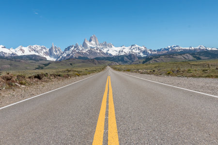 A long road with a yellow line down the middle and the Mount Fitz Roy at the background.