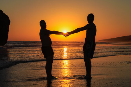 a gay couple poses on the beach at sunset