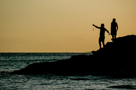 Silhouette of father and son fishing on the beach at sunsetの写真素材