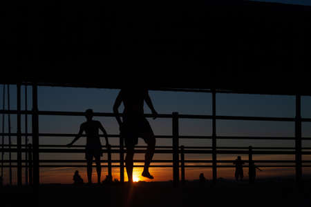 Silhouette of people playing soccer at sunset in a port.の写真素材