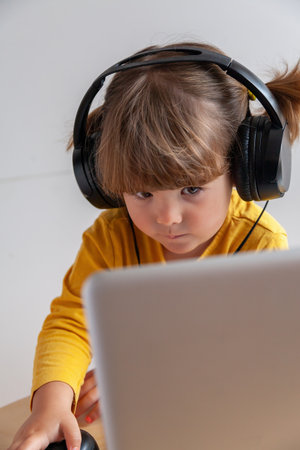 Real Cute little girl with headphones using a laptop computer at home.