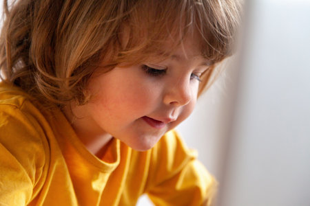 Real Little girl playing with a digital tablet in a bright yellow t-shirtの写真素材