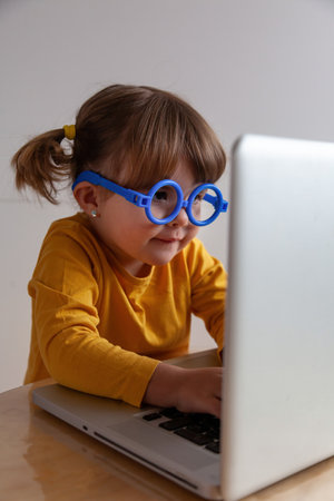 Portrait of a real cute little girl with glasses using laptop at homeの写真素材