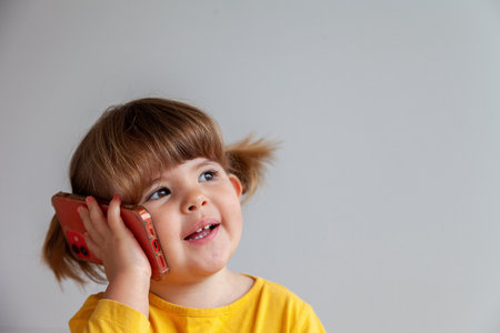 Portrait of a real cute little girl talking on the phone and smilingの写真素材