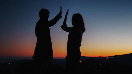 Silhouette of boy and girl high five at sunsetの写真素材
