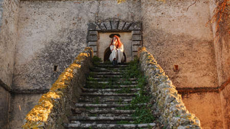 Beautiful girl with white dress sitting on the main entrance stairs of castleの写真素材