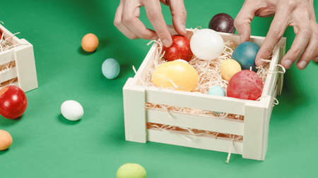 A mans hand is placing the colored Easter eggs in the basket