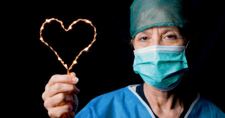 Doctor makes the symbol of the heart with mask and black background
