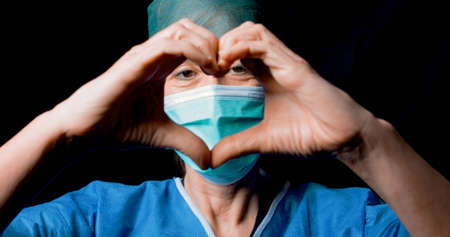 Doctor makes the symbol of the heart with mask and black backgroundの写真素材