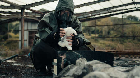 Man wearing a gas mask finds a stuffed animal in a war-torn hospitalの写真素材