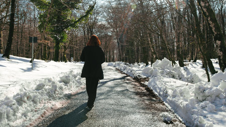 Woman walking in the street of a snowy forest in the morningの写真素材