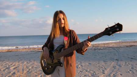 Girl Plays Bass Music Instrument On The Beach At Sunset Near Oceanの写真素材