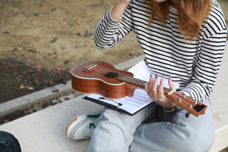 Girl Writes Notes On A Sheet Music To Play Them With The Ukuleleの写真素材