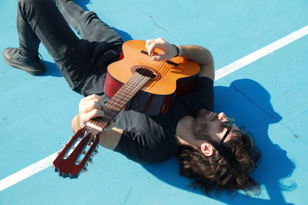 Man Lying On The Ground Plays Guitar On Blue Floor Outdoor
