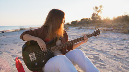 Girl Plays The Bass Instrument Sitting On The Beach At Sunset Near The Oceanの写真素材
