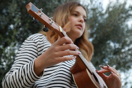 Girl Strums With Ukulele Musical Instrument Near A Tree In The Mountains