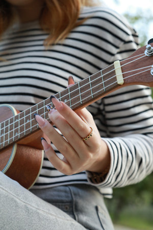 Young Woman Tunes The Ukulele Musical Instrument In A Park Outside