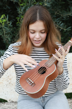 Young Woman Tunes The Ukulele Musical Instrument In A Park Outsideの写真素材